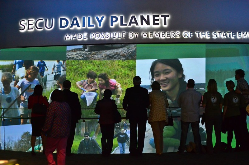 Group of people looking at the giant screen inside the SECU Daily Planet with projected images of people in nature